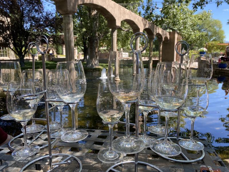 Multiple white wine tasting flights from Casa Rondeña sit on a table in front of a pond.
