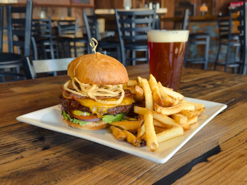 A craft BBQ burger with a side of fries and a glass of beer from Flatiron Bites and Brews.