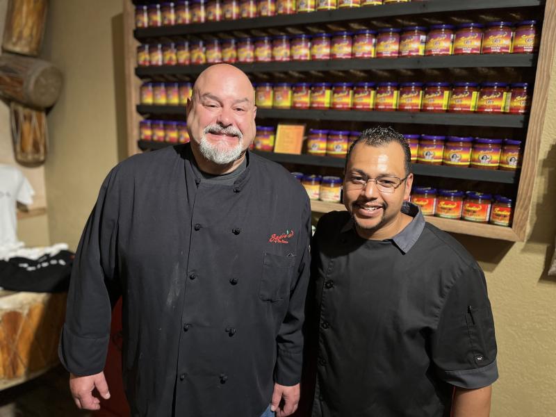 Brian Stafford and Keith Dominguez stand in front of a large shelf of salsa at Sadie's
