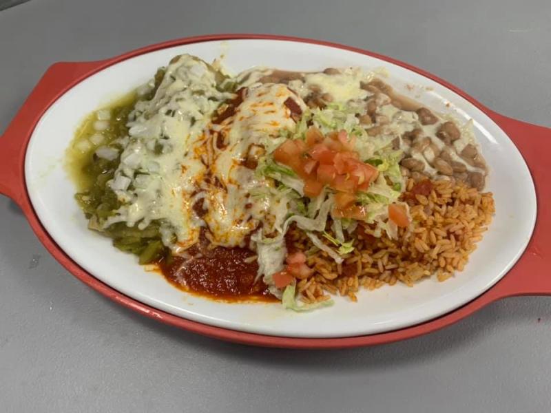 a plate of new mexican food smothered in red and green chile with rice and beans on the side