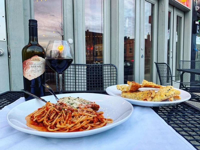 Two dinner plates and a bottle of wine on a patio table at Grazie Italiano