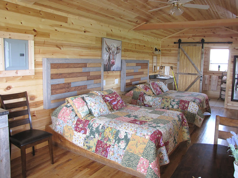 Interior of a cozy cabin room at Terry Bison Ranch with twin beds, quilted bedspreads, wooden walls, and rustic decor, including a painting of a bison.