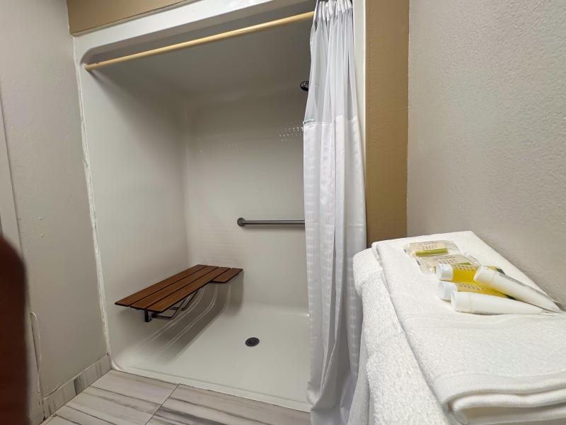 Accessible hotel bathroom featuring a roll-in shower with grab bars, built-in bench seating, and accessible amenities for guests with mobility needs.