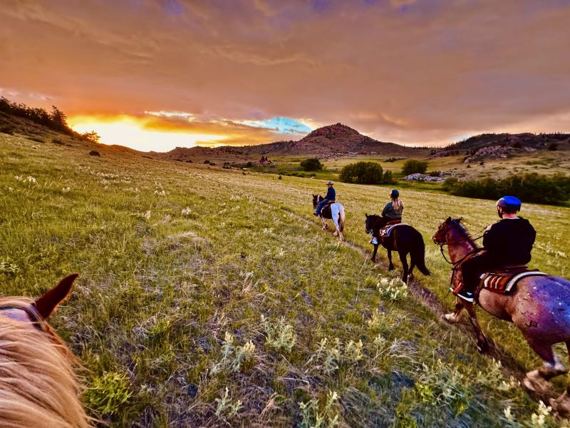 looking between horses ears of sunset and other riders riding through grassy mountains