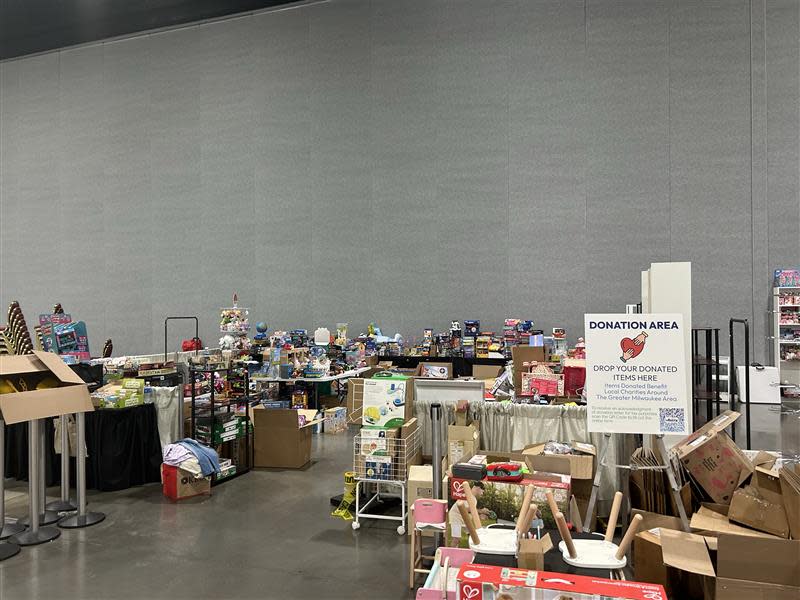 Wide view of a donation area containing stacks of donated toys, board games, puzzles and boxed products arranged on tables and carts. A donation sign stands near the center of the collection space.