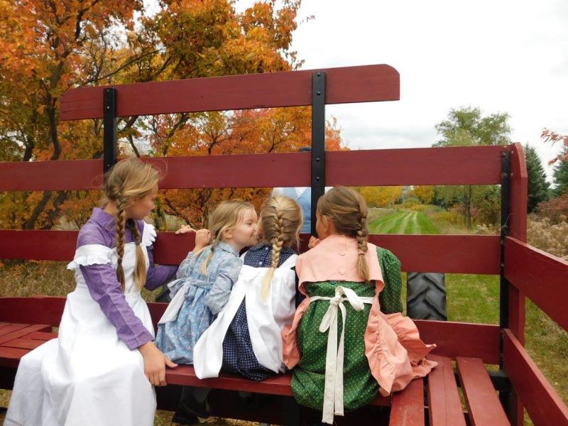 Four little girls dressed in early 1900s outfits ride in the back of a wagon during Fall on the Farm at Historic Eidem Farm