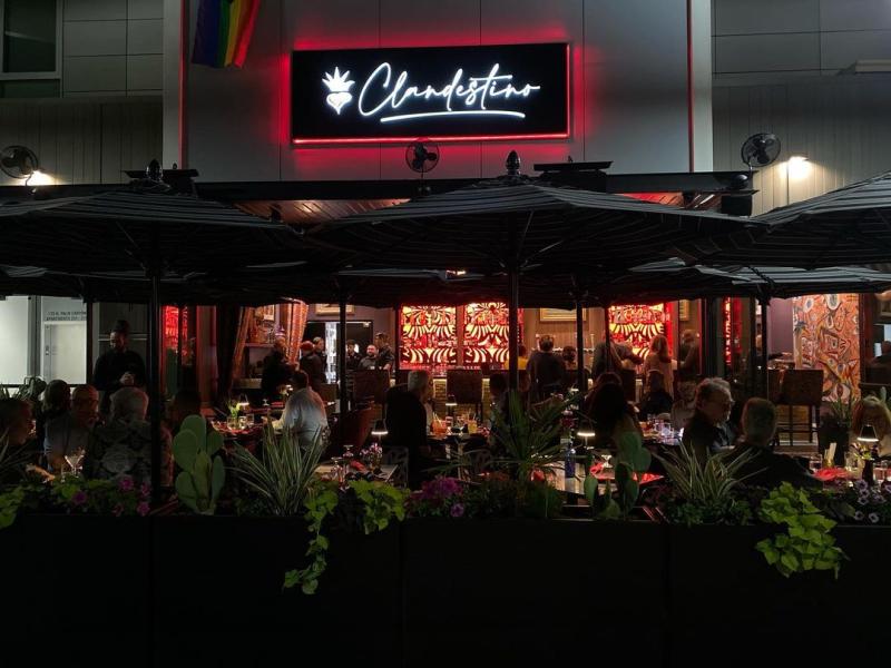 Outside patio of Clandestino restaurant in Palm Springs at night with sign lit up.