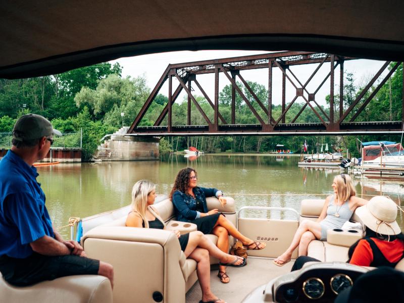 Group riding on a pontoon boat under a bridge.