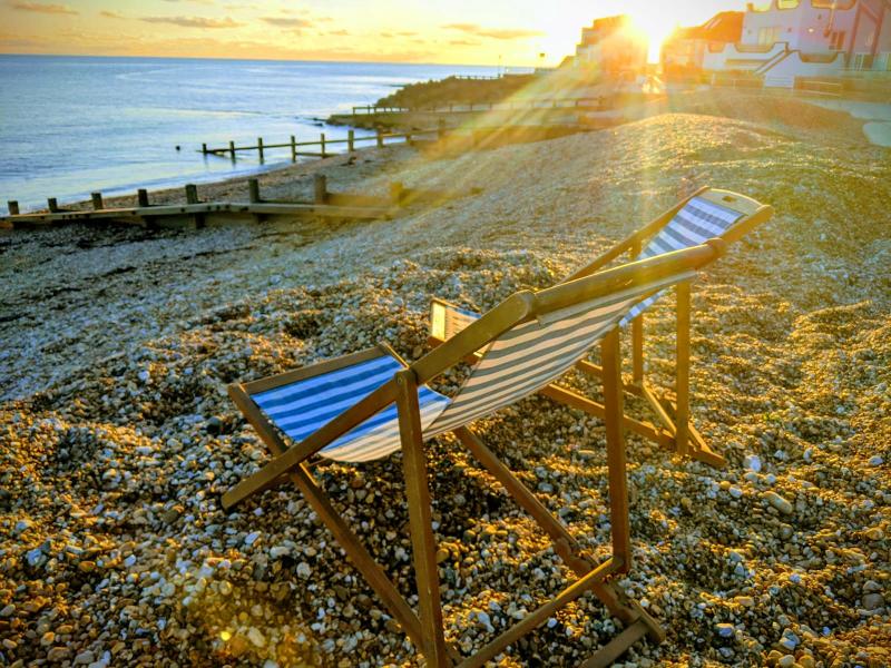 Pair of blue and white striped empty deckchairs on the shingle beach at Felpham, Sussex