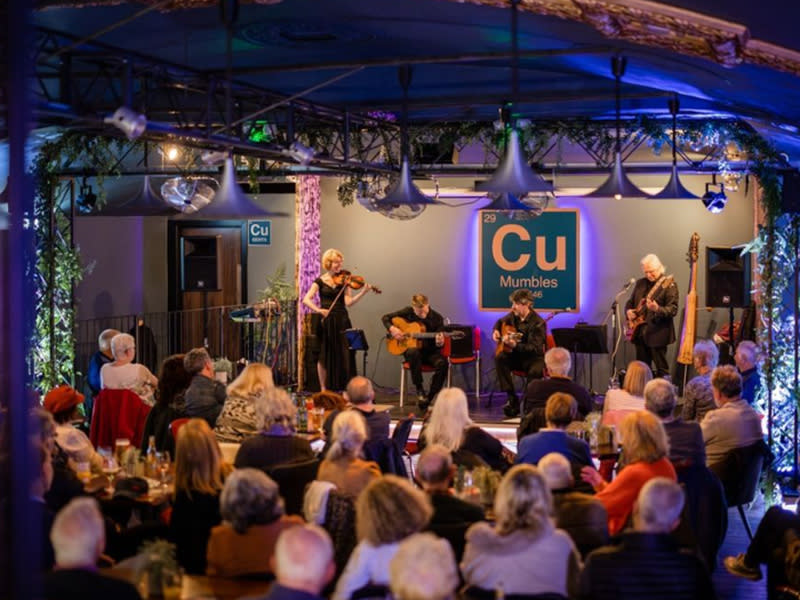 A jazz band playing on stage to a packed room in the current day.