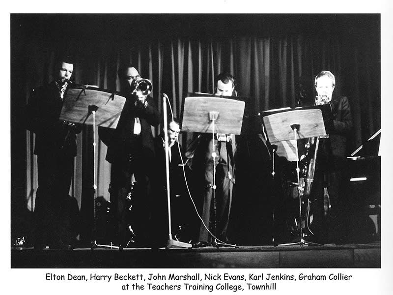 Black and white photo of fur musicians playing behind music stands on a stage.