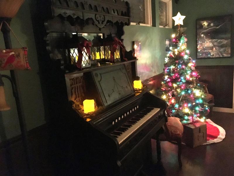piano next to a lit Christmas tree