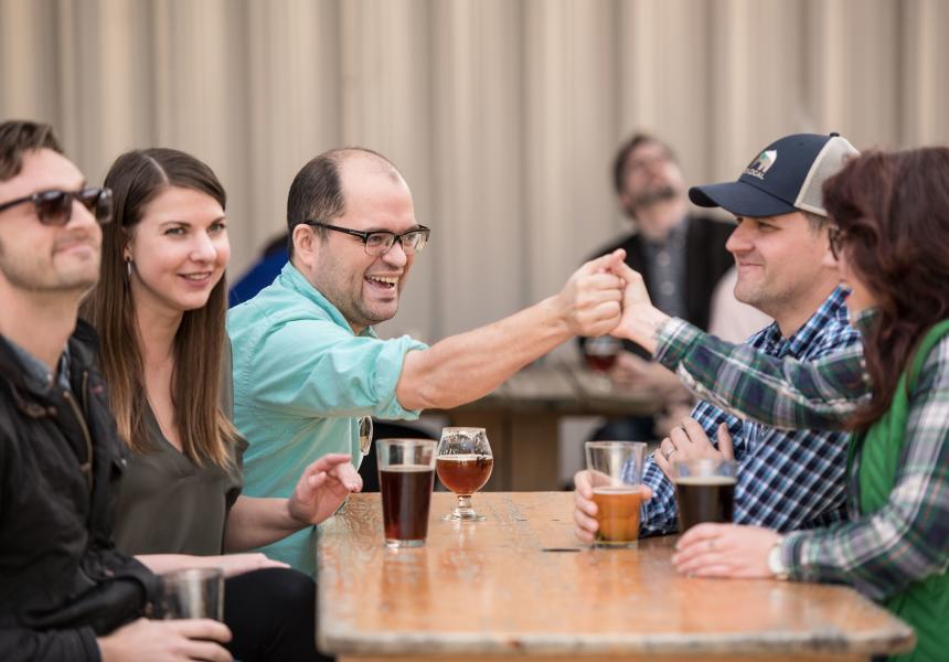 Friends handshaking over beers at an outdoor table at River Rat
