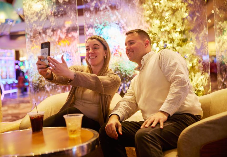 Two people taking a selfie at a bar in a casino with bright lights surrounding them