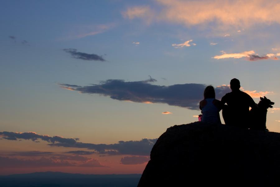 A couple sits with their dog as the sun sets