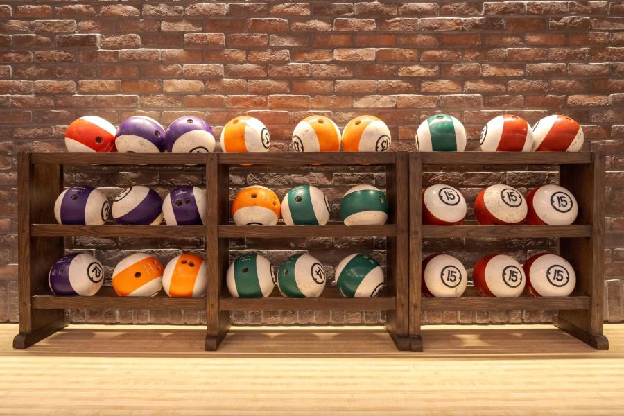 Colorful bowling balls arranged on wooden shelves against a rustic brick wall, creating a vibrant and inviting atmosphere for leisure activities.