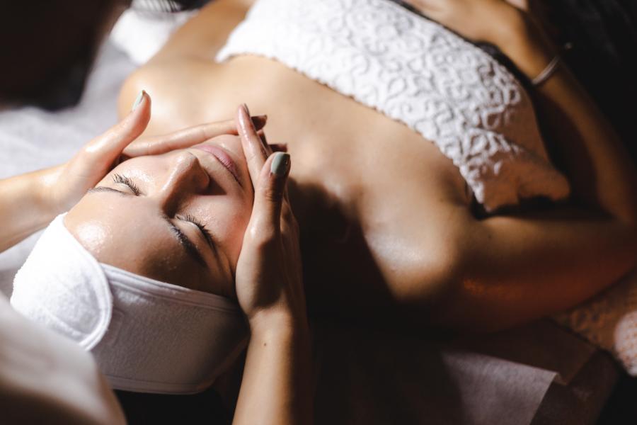 A woman receives a facial treatment in a serene spa setting, with a therapist gently massaging her face. Soft lighting enhances the relaxing atmosphere.