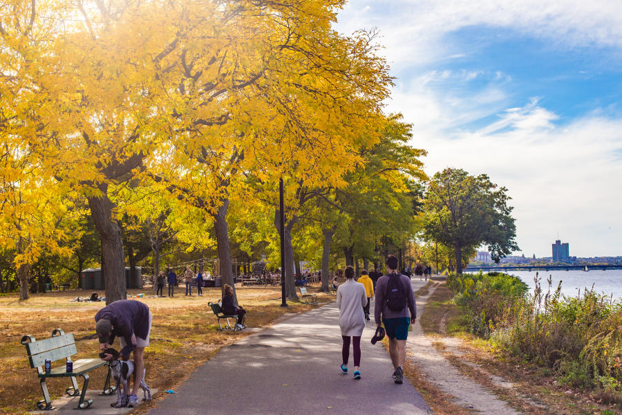 People sitting on benches and others walking on paved path along the Charles River Esplanade of Boston