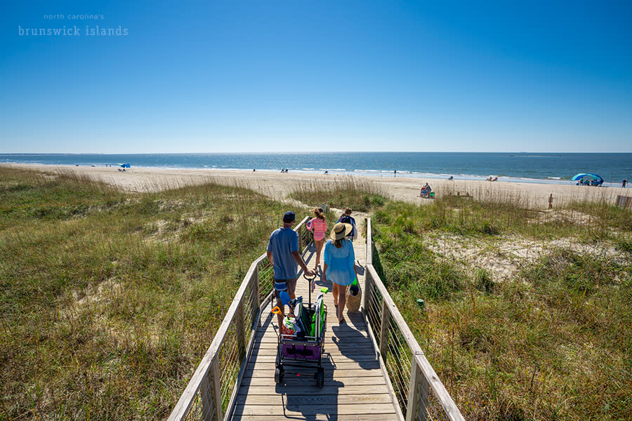 a family of 4 walking out to the beach on a wooden walkway pulling a beach wagon