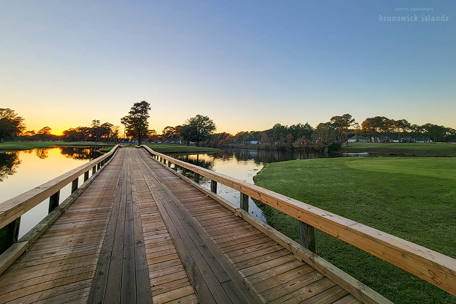 a wooden bridge over water running along a golf course