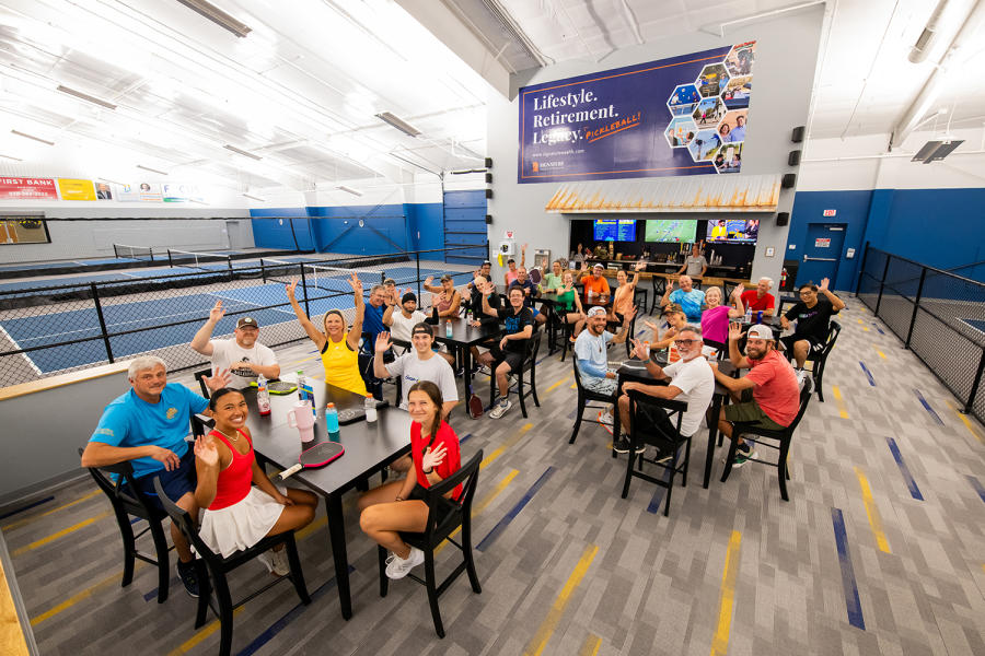 a large group of pickleball players waving to camera