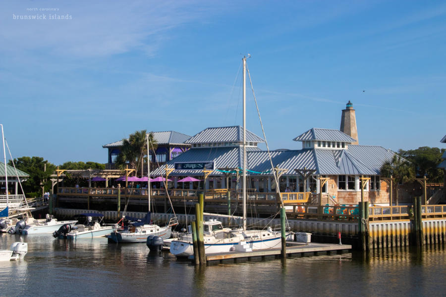 a large waterfront restaurant with boats docked in front and a lighthouse visible in the background
