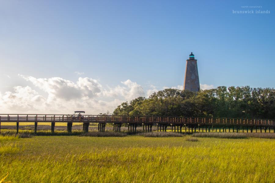 a view of a golf cart traveling over a bridge over marshland with a lighthouse in the background
