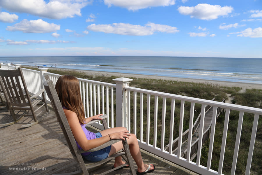 a girl sitting on a rocking chair on a deck of a vacation rental house on the beach