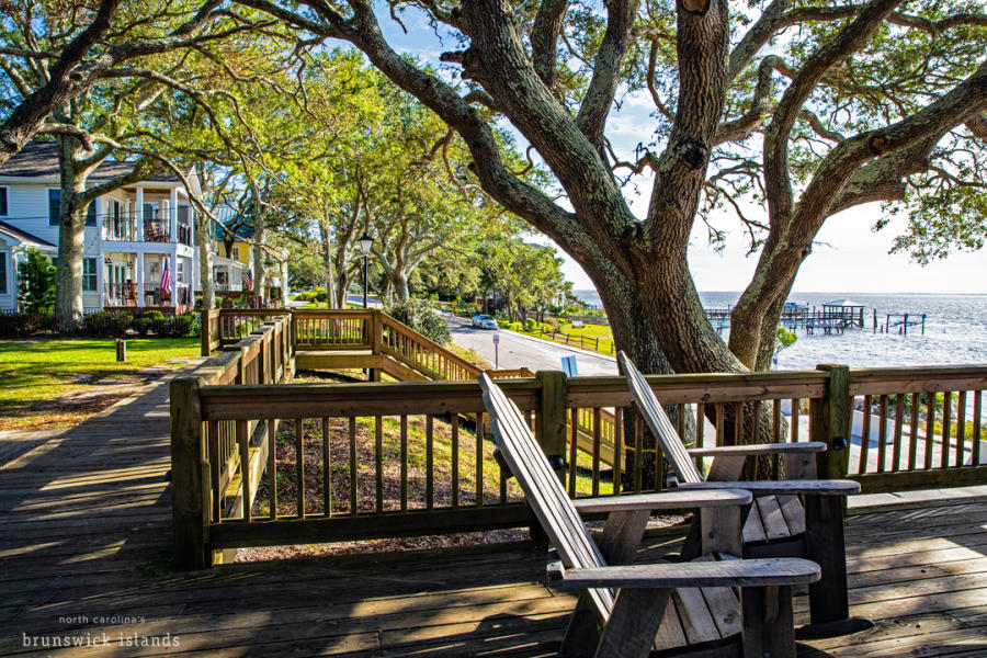 two wooden chairs on a wooden deck overlooking a road and the Cape Fear River below in Southport NC
