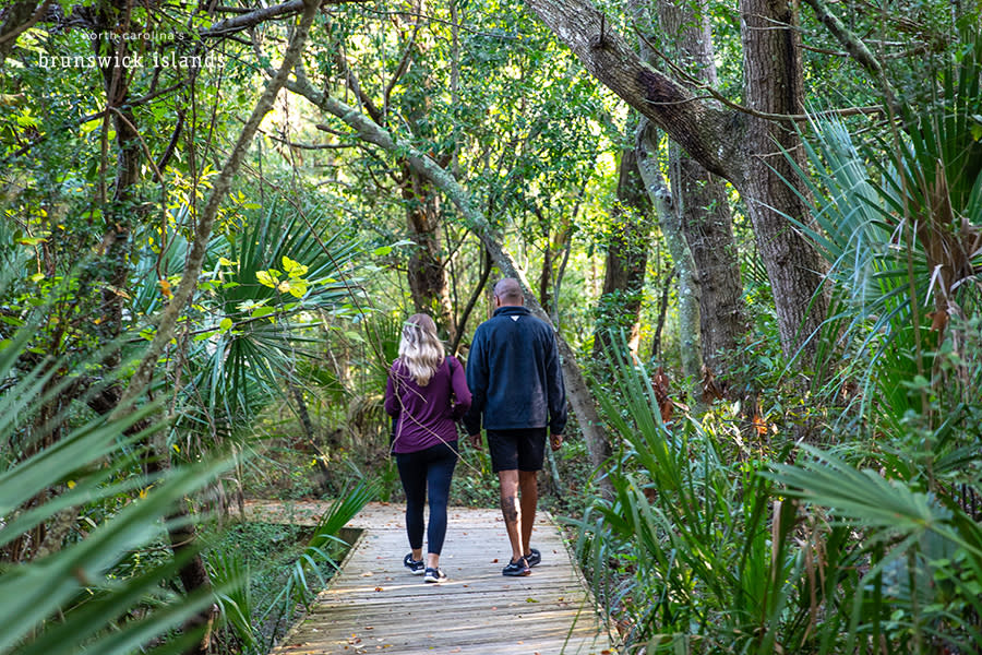 a couple walking down a wooden path in a tropical forest