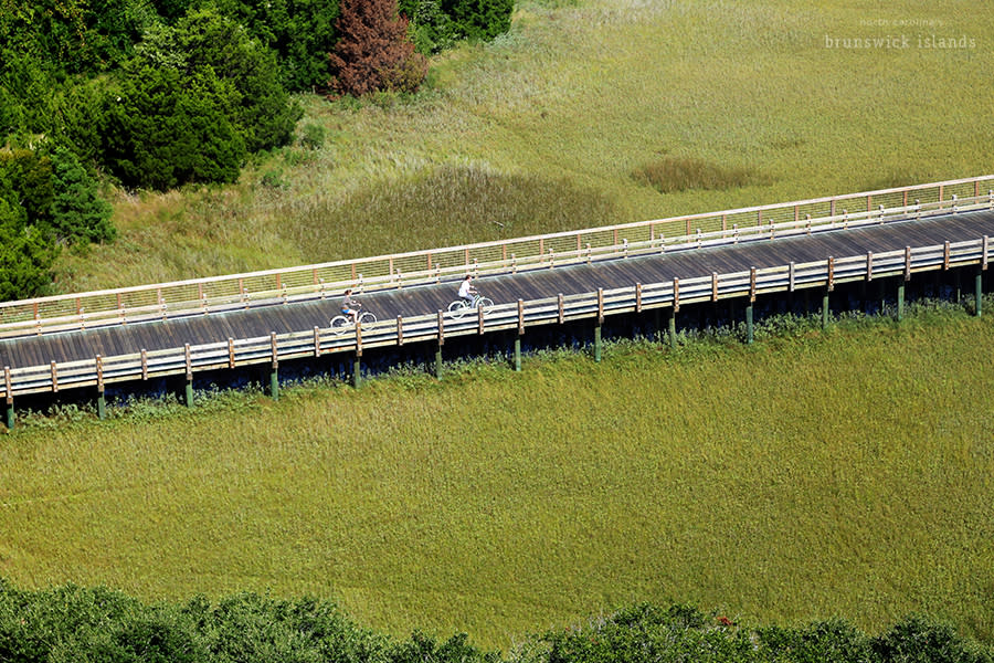aerial view of two people biking on a wooden bridge over a marsh on bald head island