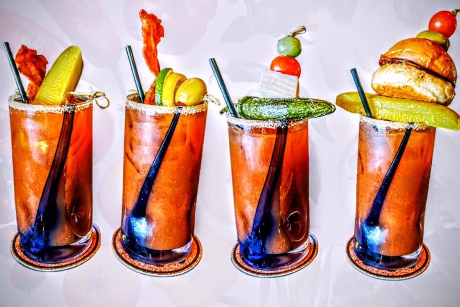 four Bloody Marys with toppings including pickles, mini burger, bacon slices, cheese and veggies