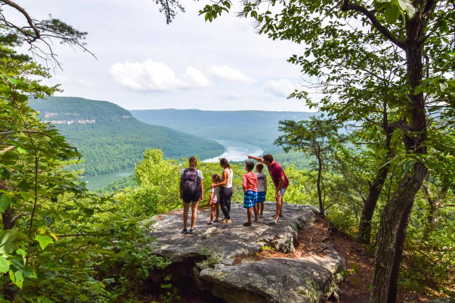 family stands on rock at cliff overlooking river and valley