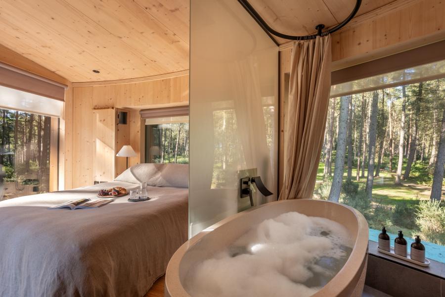 Trees are visible through windows of a treehouse, which has a bubble-filled slipper bath and large bed, at Treedwellers