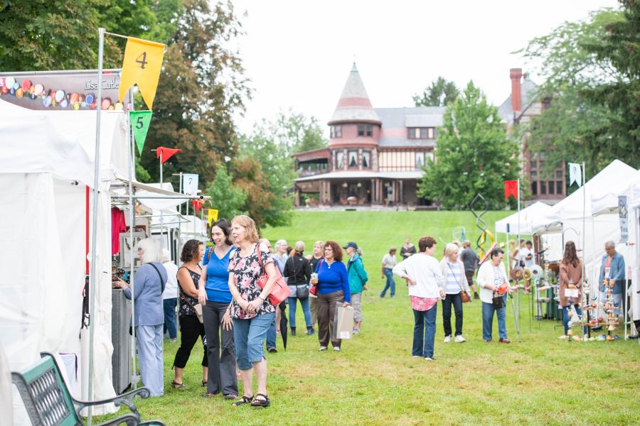 People browsing art vendors' stalls in the gardens of Sonnenberg Gardens State Historic Site, with the mansion in the background.