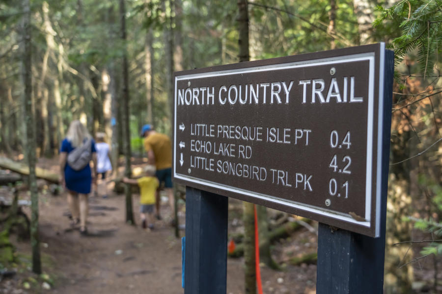Signage on the North Country Trail with a family walking on the path in the background