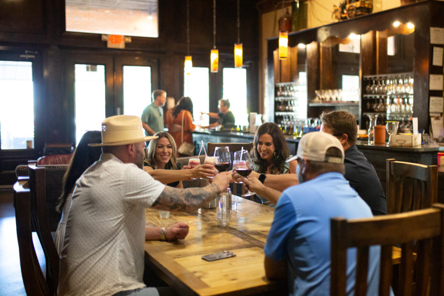 Men and women around a table in a winery, toasting with wine glasses