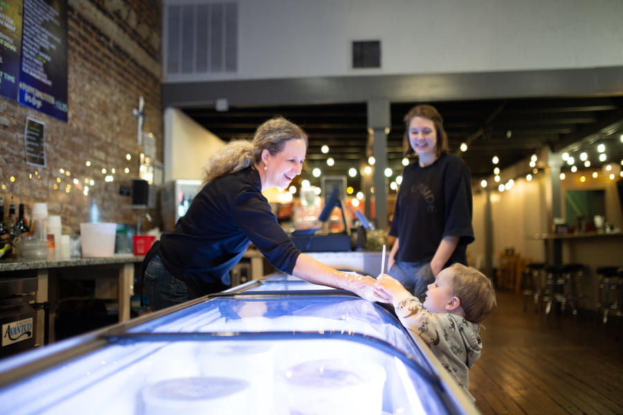 Woman leaning over the ice cream counter handing a cup of ice cream to a small child