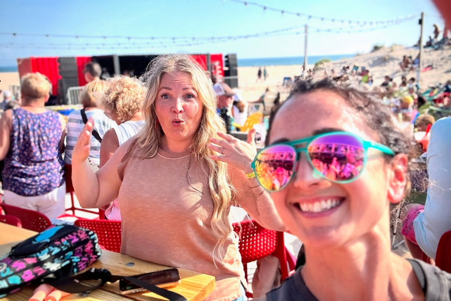 Two people enjoying a sunny day at a beach restaurant with a red stage in the background, expressing excitement and happiness.