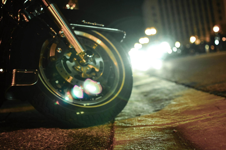 front tire of motorcycle in foreground with headlights from oncoming bikes illuminating the background
