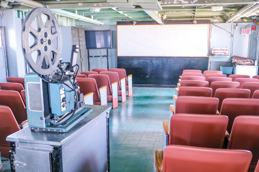 vintage movie projecter sits in aisle between art deco style theatre chairs