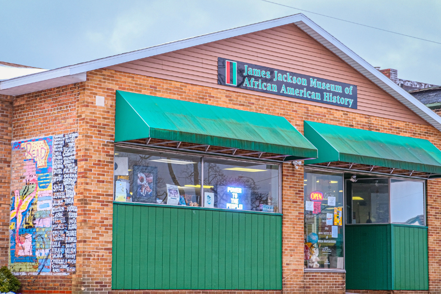 A brick building with green awnings and a sign reading "James Jackson Museum of African American History." A colorful mural and "Open" sign are visible.