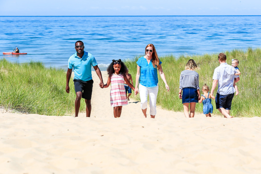 Group of people enjoying a sunny day at the beach, with some walking on the sand and others playing near the water.
