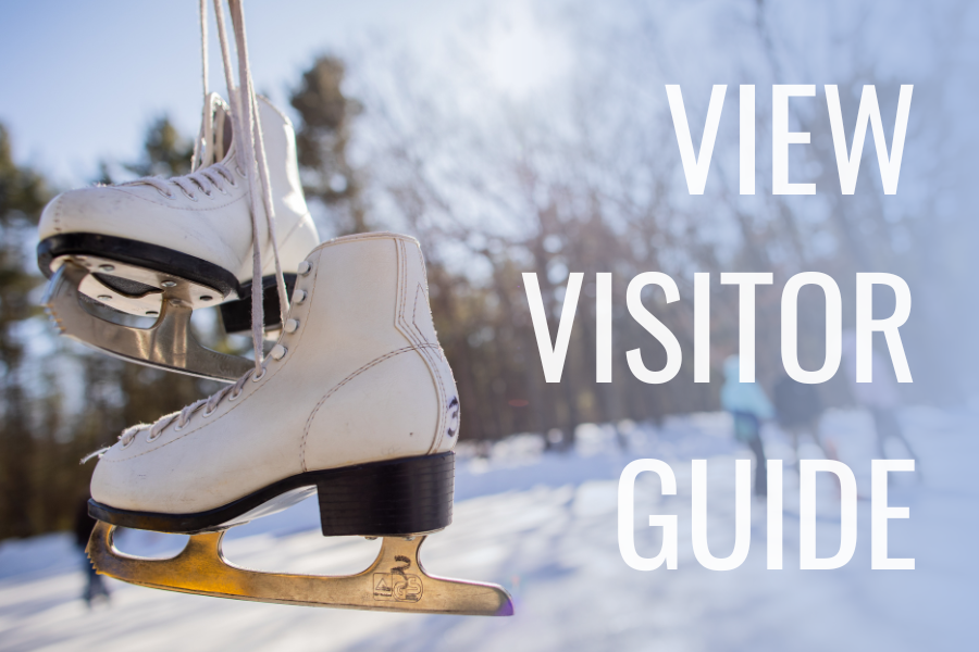A pair of white ice skates hanging by laces in a snowy outdoor setting with blurred trees in the background. Text reads, "View Visitor Guide."
