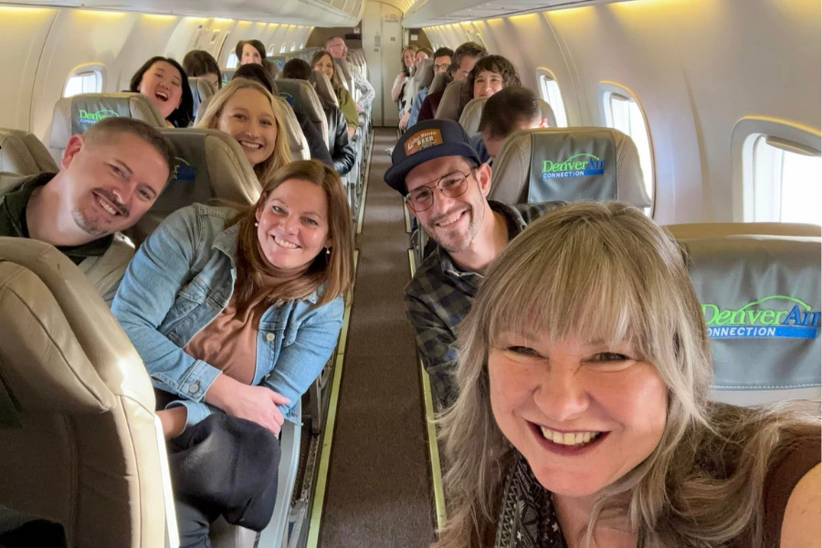 Group of passengers smiling and posing for a selfie inside a Denver Air Connection airplane cabin.