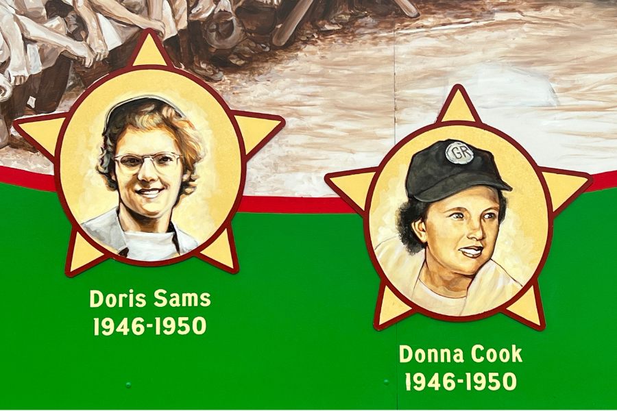 Portraits of Doris Sams and Donna Cook, each set within a star, displayed against a background depicting a baseball scene. Dates under each name read 1946-1950.