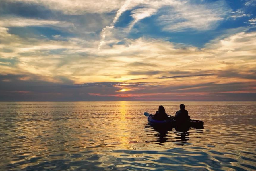Two people kayaking on a calm Lake Michigan at sunset with vibrant sky colors.