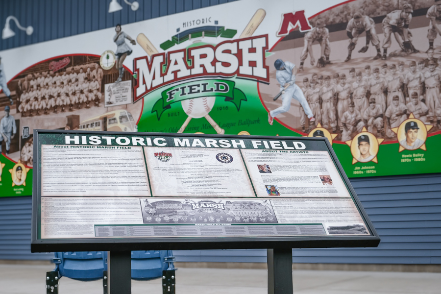 Information panel at Historic Marsh Field detailing the history of the baseball park, with mural displayed in the background.