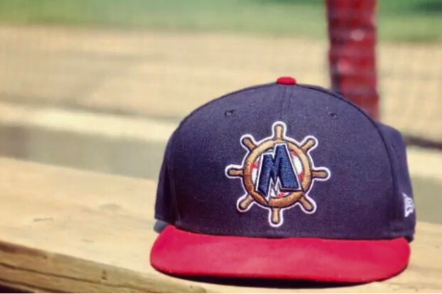 A Muskegon Clippers baseball cap with a dark blue crown and red brim, featuring an embroidered logo of a compass with an "M".