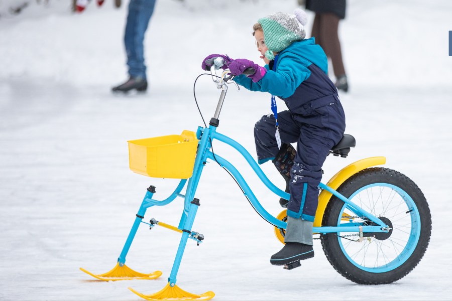 A child rides a blue and yellow ice bicycle on a snowy surface.